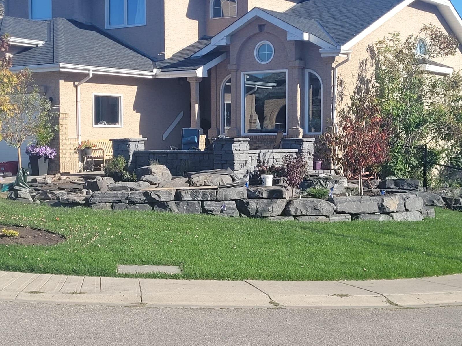 Armour-stone boulder retaining wall and front-yard landscaping at a Calgary-area home by Sungreen.